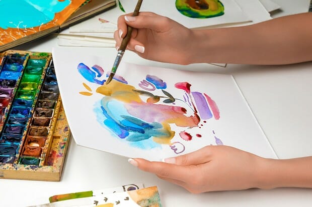 selective focus of female hands drawing on paper with watercolor paints and paintbrush